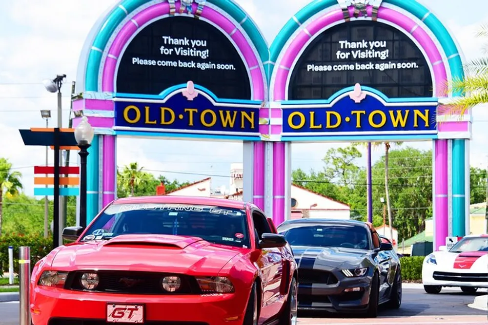 A red Mustang GT takes the lead under a colorful Old Town archway with a message thanking visitors as other cars follow