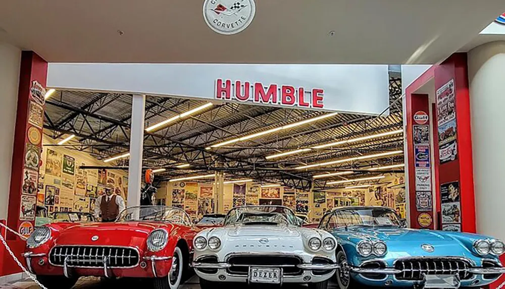 The image shows a vintage-themed exhibit featuring classic Chevrolet Corvettes in red white and blue with a HUMBLE sign displayed prominently above the cars