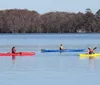 Two people are kayaking on a calm blue lake under a clear sky