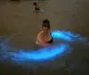 People are kayaking at dusk with illuminated kayaks that cast a blue glow on the water