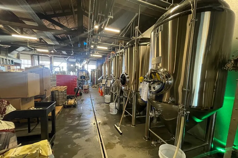 The image shows the interior of a brewery with stainless steel fermenting tanks and brewing equipment