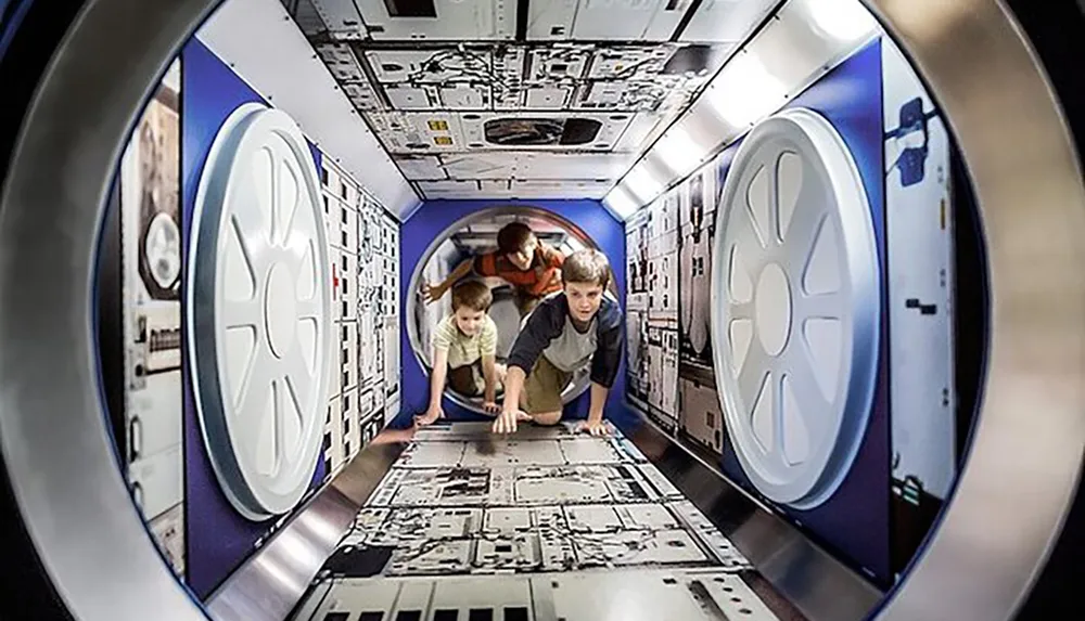 Three people are crawling through a tunnel-like structure designed to resemble the interior of a futuristic spacecraft