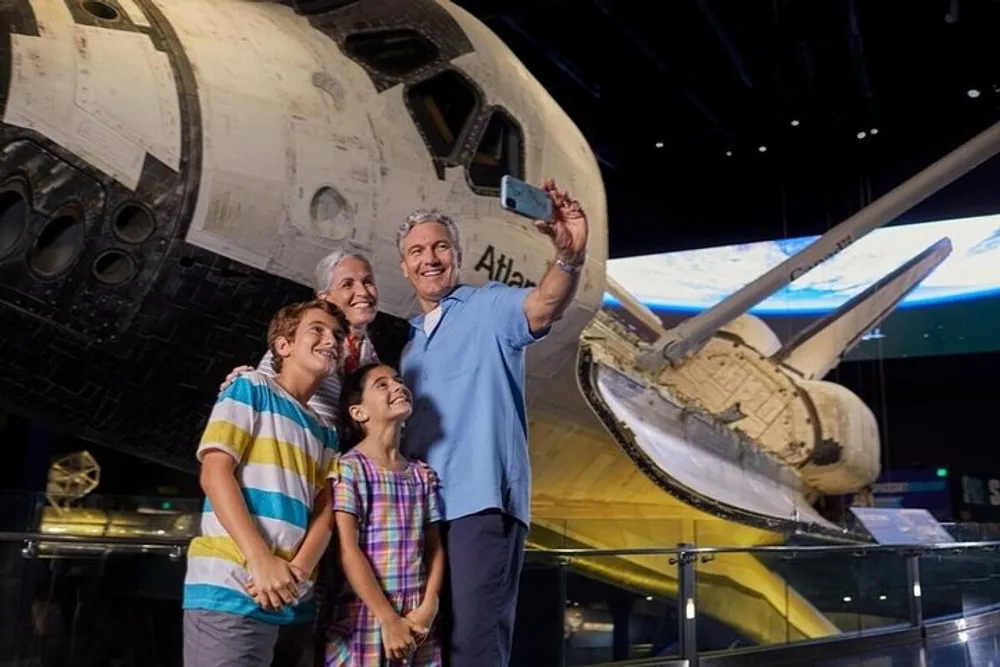 A family is happily taking a selfie with the Space Shuttle Atlantis exhibit in the background