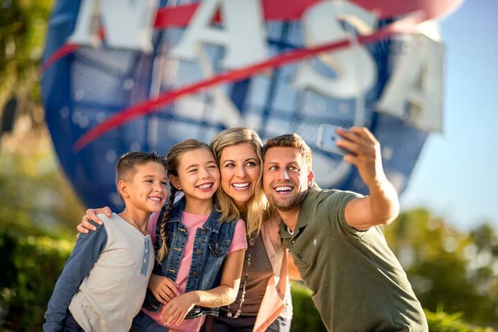 A happy family is taking a selfie in front of a large NASA sign on a sunny day