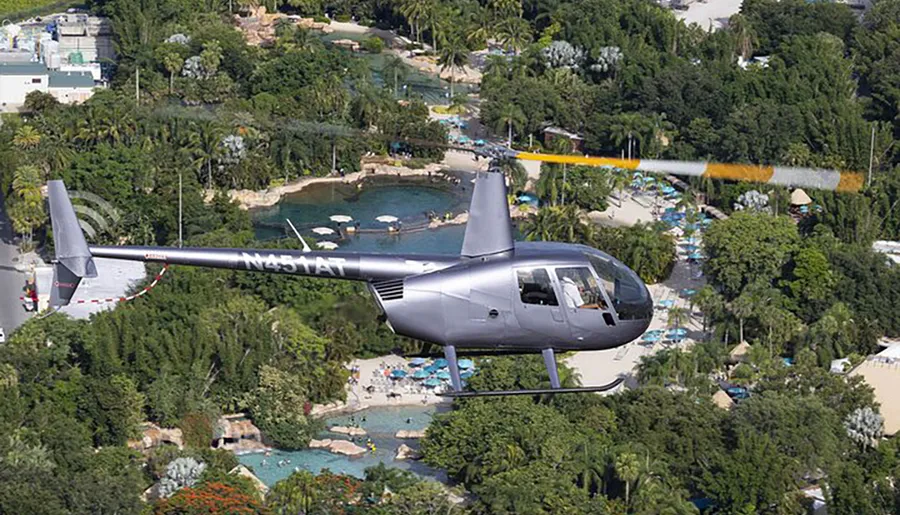 A helicopter is flying over a tropical resort area with pools and lush greenery.