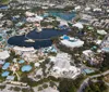 The image is an aerial view of a large resort complex featuring multiple buildings with colorful rooftops swimming pools and spacious parking areas amidst greenery