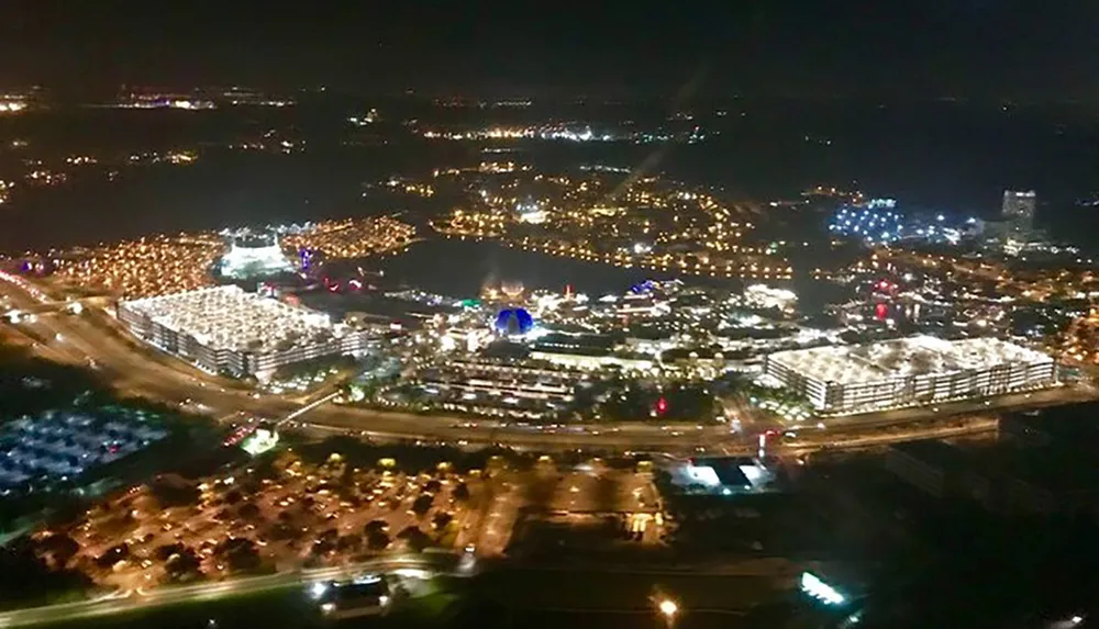 An aerial nighttime view shows a brightly lit urban area with dense buildings roads and various sources of illumination