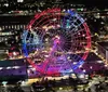 An illuminated Ferris wheel stands out against the night skyline casting vibrant red and blue hues over the surrounding area