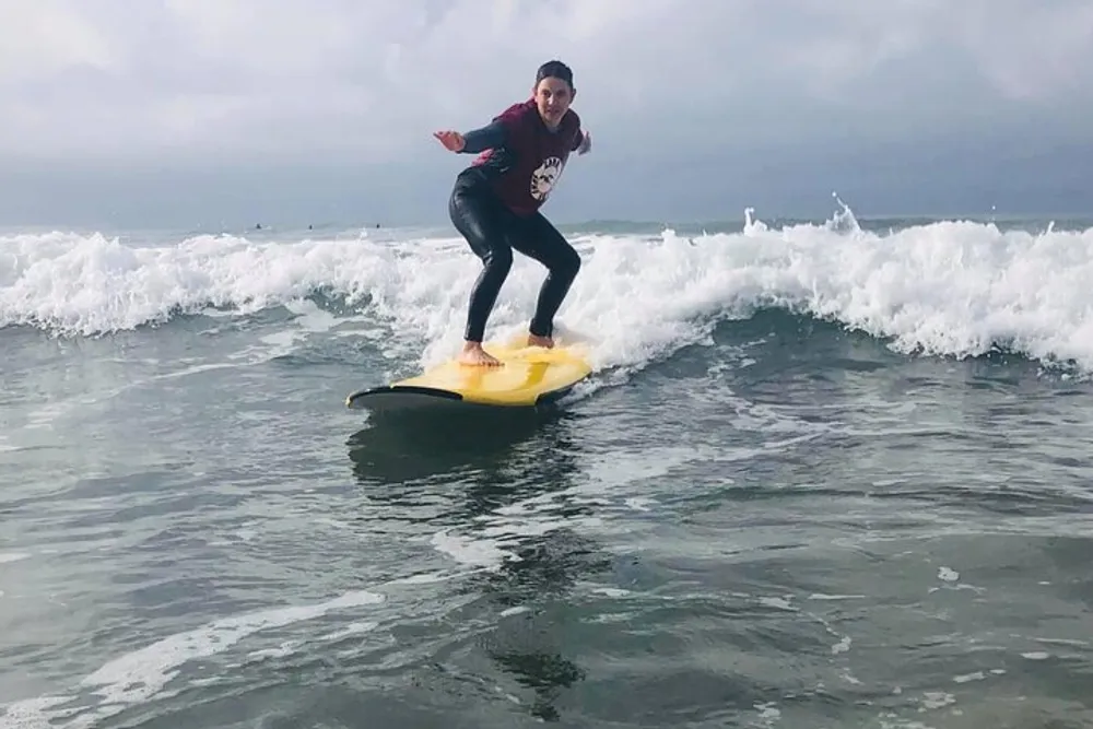 A person is surfing on a wave balancing on a yellow surfboard with grey overcast skies above them