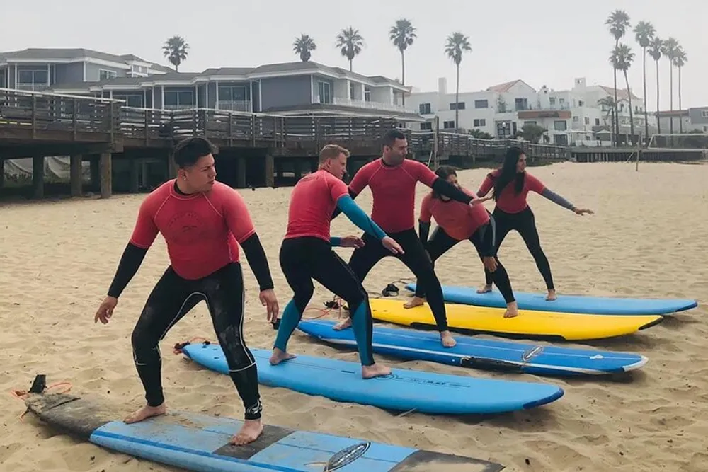 A group of individuals wearing wetsuits is practicing surfing stances on colorful surfboards on a sandy beach