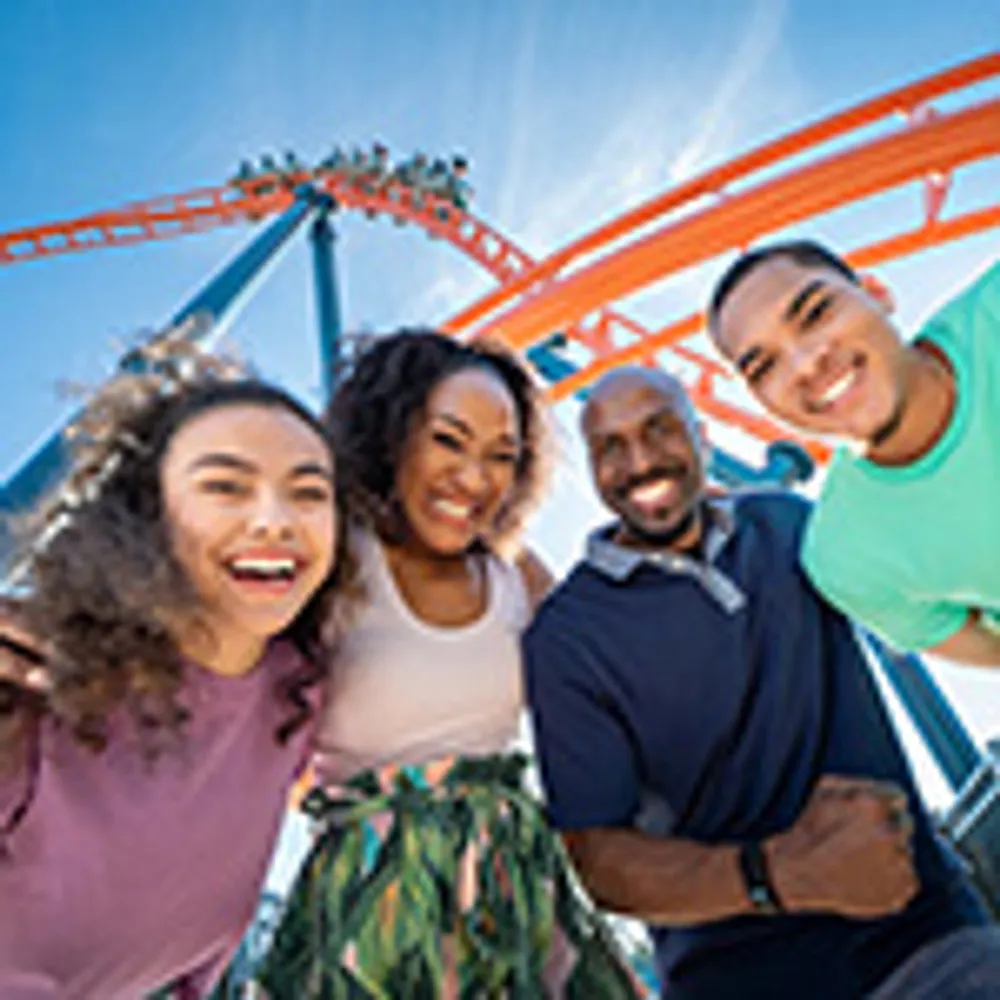 A happy family is enjoying a day at an amusement park with a roller coaster in the background
