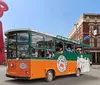 The image shows a colorful hop-on hop-off tour trolley filled with passengers in front of urban scenery featuring a distinctive red abstract sculpture