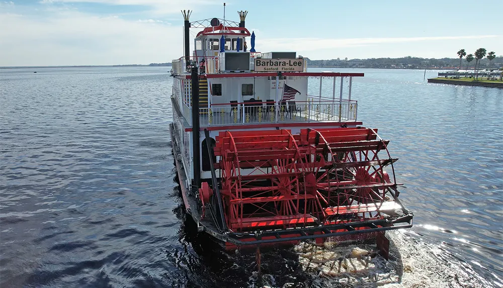 The image shows the stern of a red paddlewheel riverboat named Barbara-Lee from Sanford Florida moving through the water