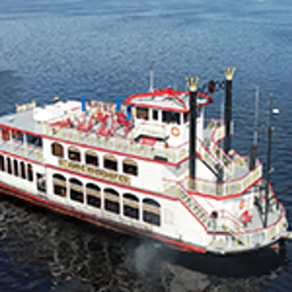 The image shows a white and red riverboat with multiple decks cruising on a body of water
