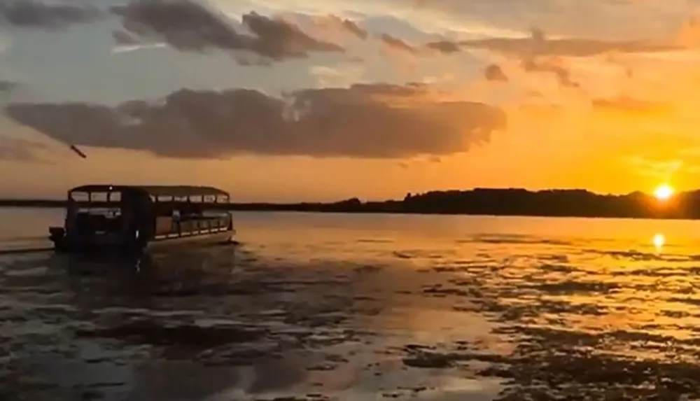 A boat sails in tranquil waters under a dramatic sunset sky