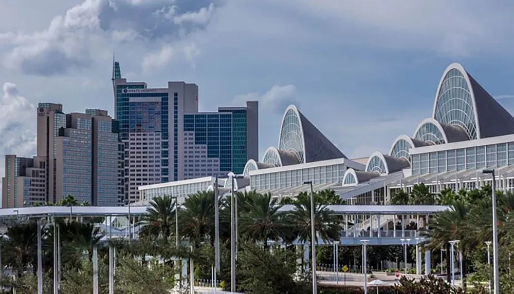 A cityscape featuring a distinctive modern building with sail-like structures flanked by conventional high-rise buildings under a cloudy sky