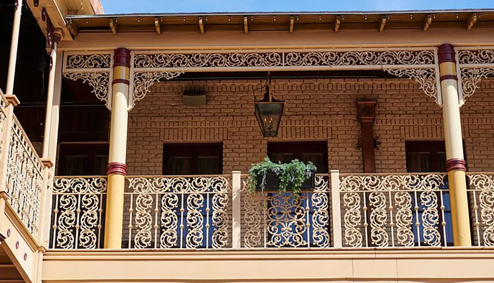 The image shows the upper level of a brick building featuring an ornate balcony with blue and white railings decorative ironwork and a hanging lantern