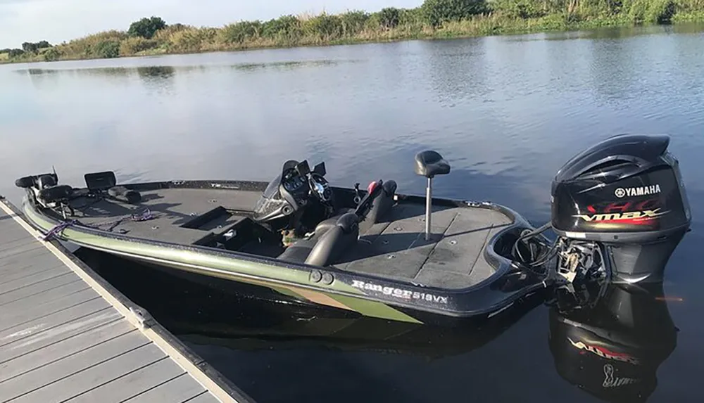 A black bass fishing boat with a Yamaha outboard engine is docked on calm waters with fishing rods and gear on board