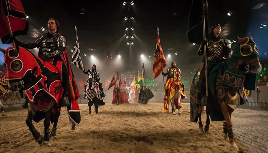 Knights in ornate medieval armor ride on elaborately dressed horses in an arena, likely during a theatrical performance or a reenactment event.