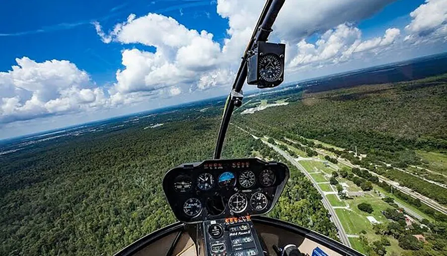 The image captures the cockpit view from a helicopter flying over a lush landscape, with an array of flight instruments visible in the foreground.
