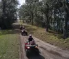 A person wearing a helmet is riding a blue ATV on a sandy trail surrounded by trees