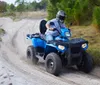 A person wearing a helmet is riding a blue ATV on a sandy trail surrounded by trees