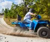 A person wearing a helmet is riding a blue ATV on a sandy trail surrounded by trees