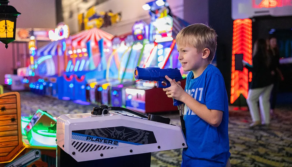 A young boy is playing a shooting game in a brightly lit arcade