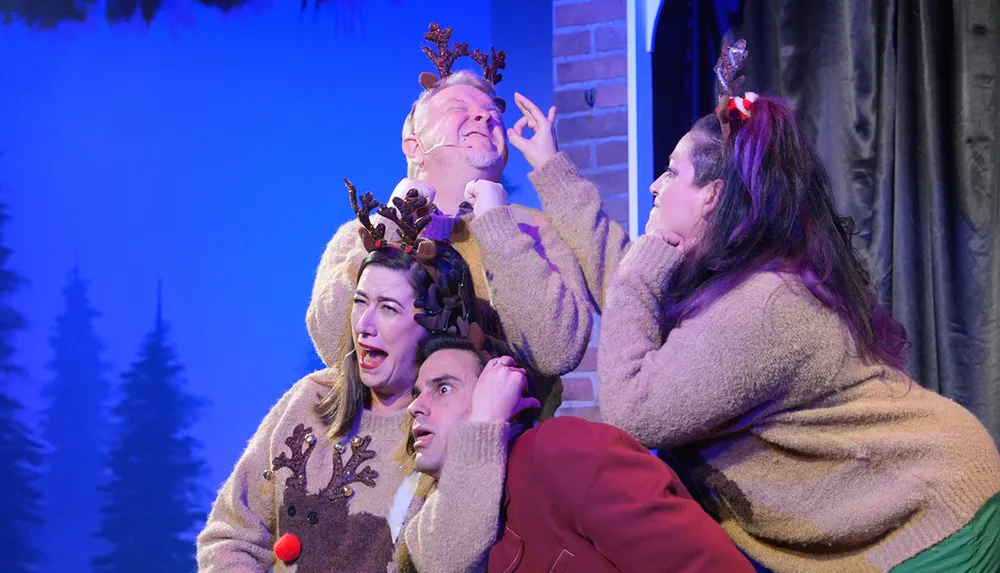 Four people wearing reindeer antlers are playfully posing with exaggerated expressions on stage