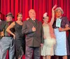 Seven people dressed in vintage formal attire stand in front of a height chart backdrop