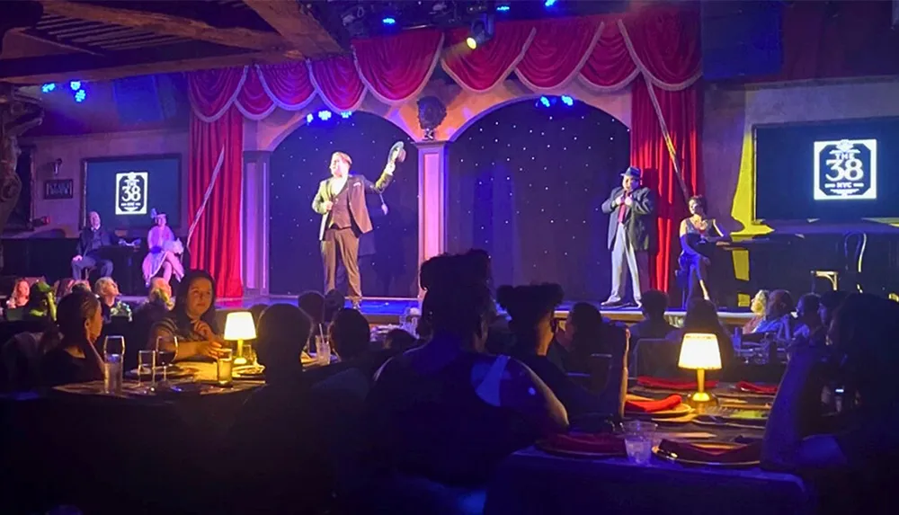 A performer is entertaining a seated audience in a dimly lit decorated venue with a stage and a cabaret-style setting