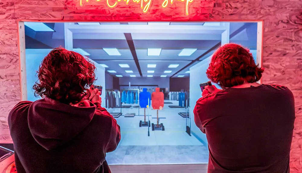 Two people are aiming at a virtual shooting range screen in a neon-lit room