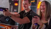Two people are joyfully playing an arcade shooting game.