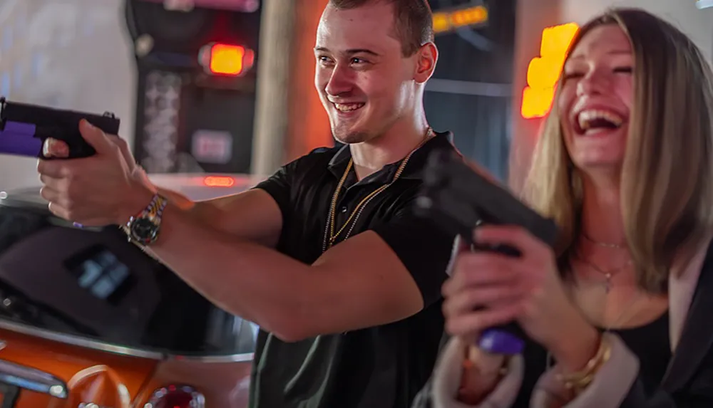 Two people are joyfully playing an arcade shooting game