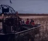 An airboat carrying passengers glides through a wetland area at twilight