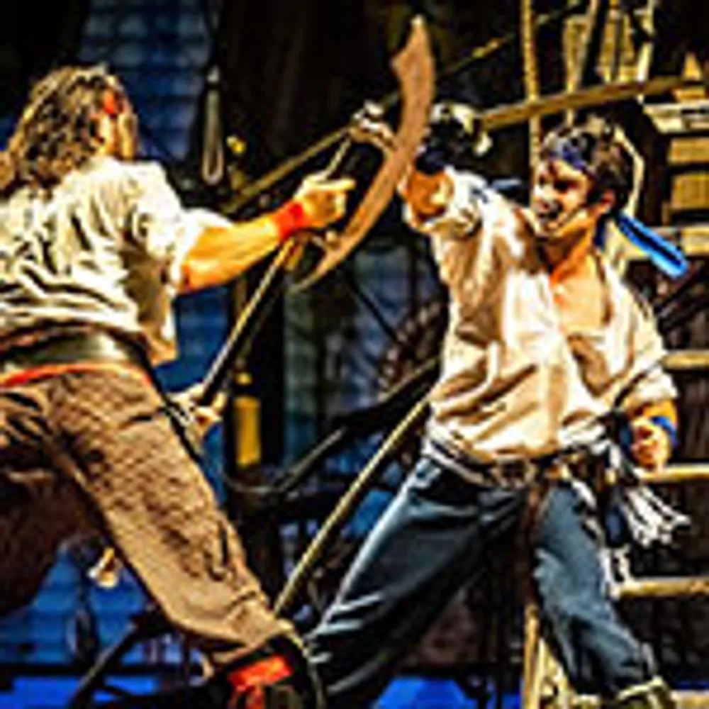 Two actors are engaged in an intense staged sword fight on a theatrical set