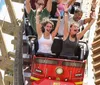 Thrilled passengers with raised arms are experiencing a steep drop on a wooden roller coaster under a clear sky