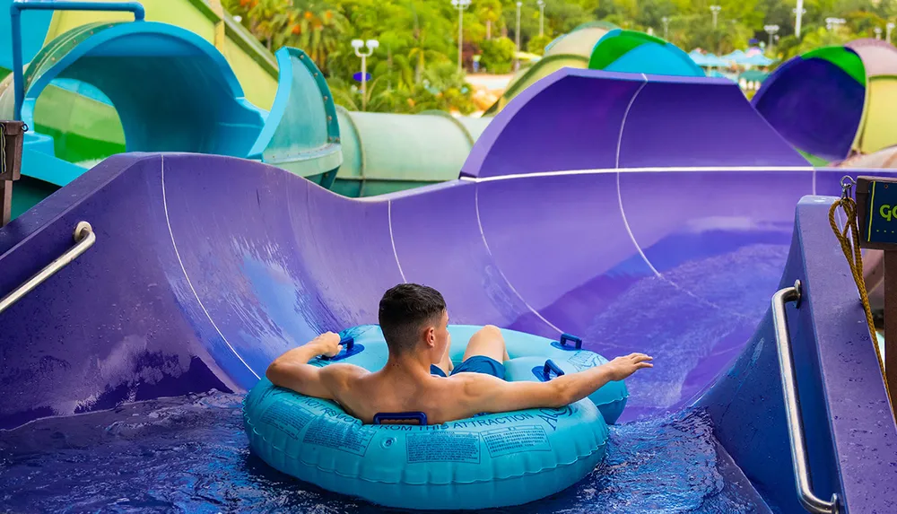 A person is preparing to slide down a colorful water slide in a water park while seated on a blue inflatable ring