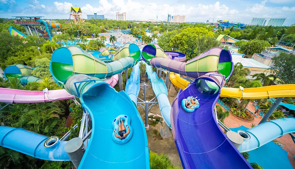 An aerial view shows people enjoying colorful water slides at a vibrant water park surrounded by lush greenery