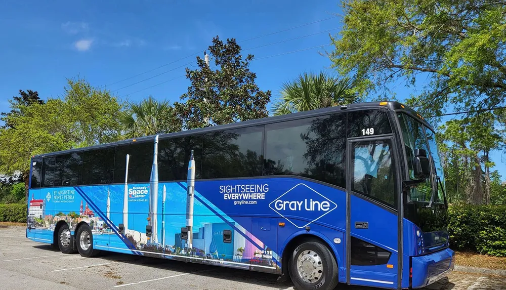 A blue tour bus with advertising wraps is parked under a clear sky with trees in the background