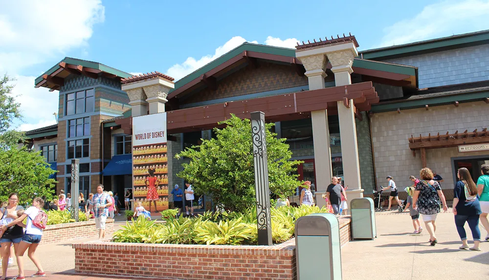 The image shows visitors walking outside the World of Disney store in a sunny outdoor shopping area with lush green plants and clear blue skies