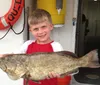 Two smiling men are posing on a boat each holding up a large fish they seemingly caught