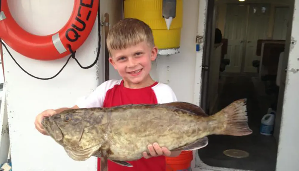 A joyful boy is proudly holding a large fish onboard a boat with life-saving equipment visible in the background