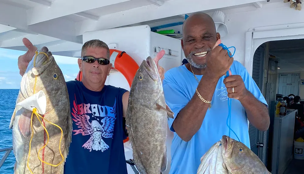 Two smiling men are posing on a boat each holding up a large fish they seemingly caught