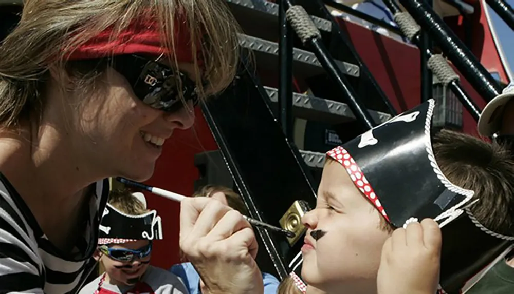 A woman is painting a mustache on a childs face both dressed as pirates creating a playful and heartwarming scene