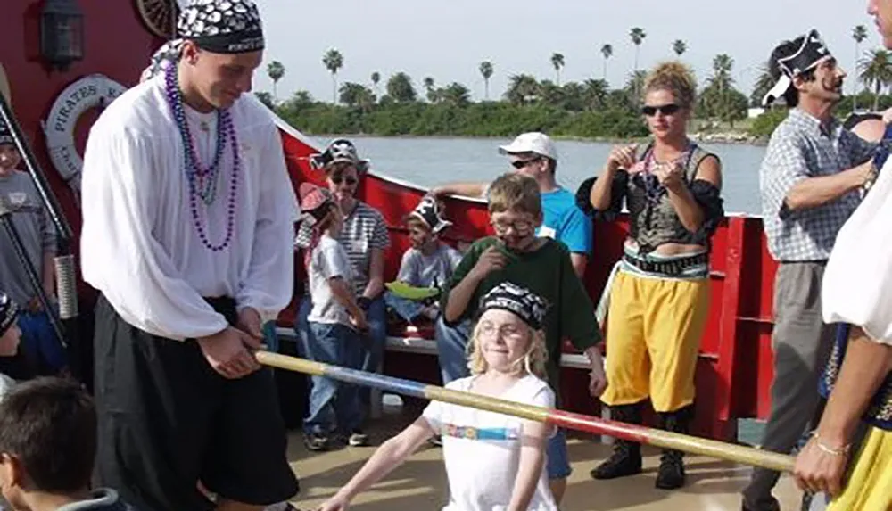 A child participates in a playful sword fighting interaction with a person dressed as a pirate surrounded by other people in pirate attire and casual clothes on what appears to be a themed boat tour