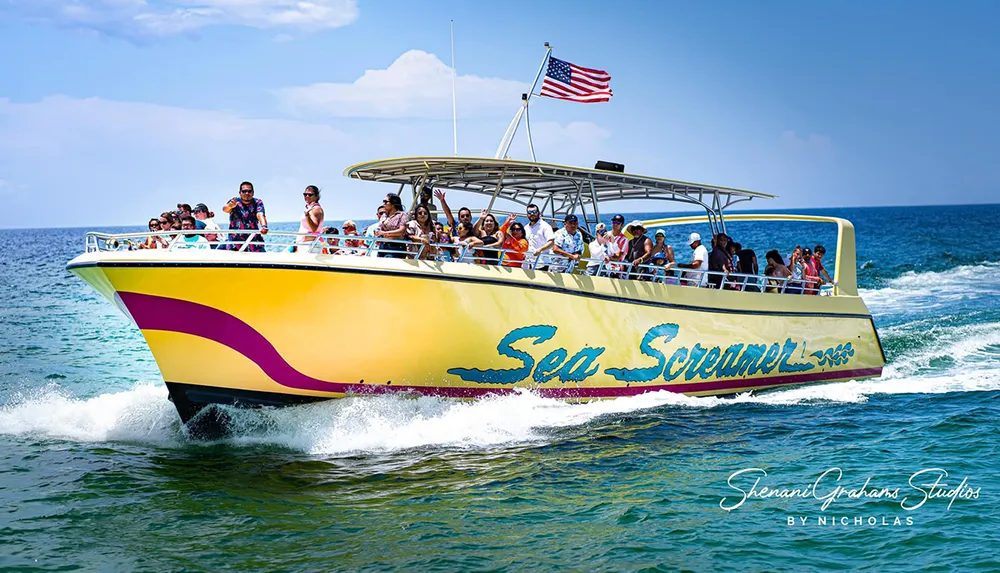 A group of people enjoys a sunny day on a speeding yellow boat named Sea Screamer on the water with an American flag flying at the stern