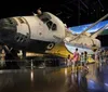 A boy in an astronaut costume holds a toy space shuttle with wide-eyed awe while a girl looks on both in front of a backdrop of what appears to be a real spacecraft