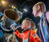 A boy in an astronaut costume holds a toy space shuttle with wide-eyed awe while a girl looks on both in front of a backdrop of what appears to be a real spacecraft