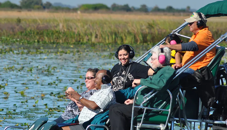 A group of people wearing headphones are enjoying a boat tour on a lake surrounded by vegetation.